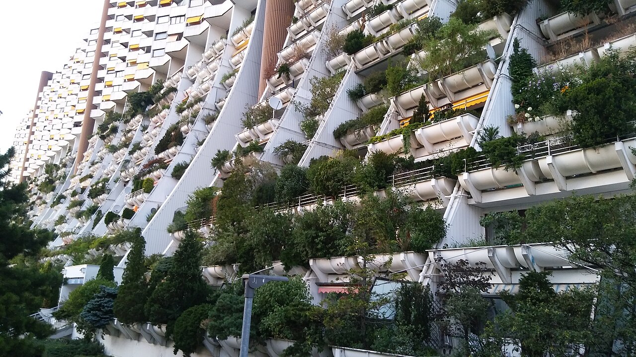 Close view of Alterlaa from the ground, multiple 27 story housing units, the lower 12 floors have set back terraces with large planters allowing for a lot of greenery.