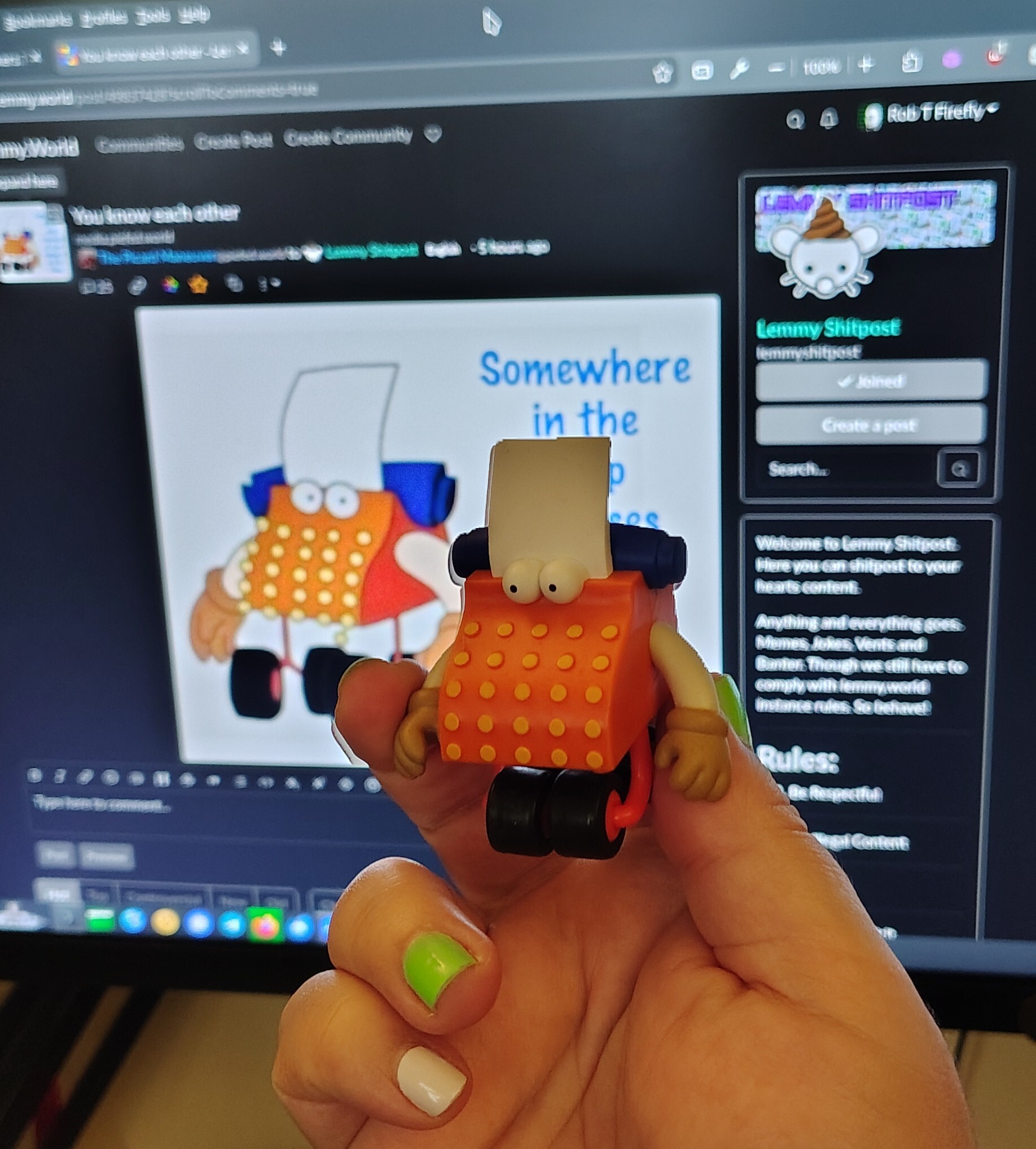 Photo of my hand holding up an action figure of the Sesame Street typewriter guy in front of my screen showing this very post about him.