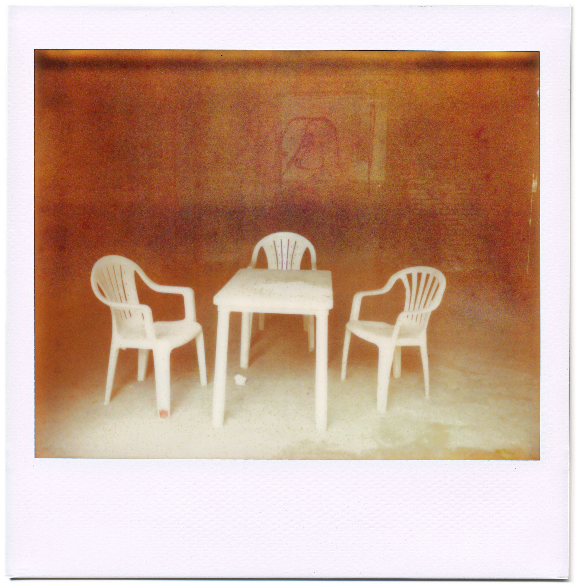 Spooky misprocessed grainy analog nighttime photo of 3 white monobloc garden chairs around a generic plastic table