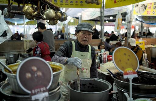 Older Korean man at a market preparing food for his customers